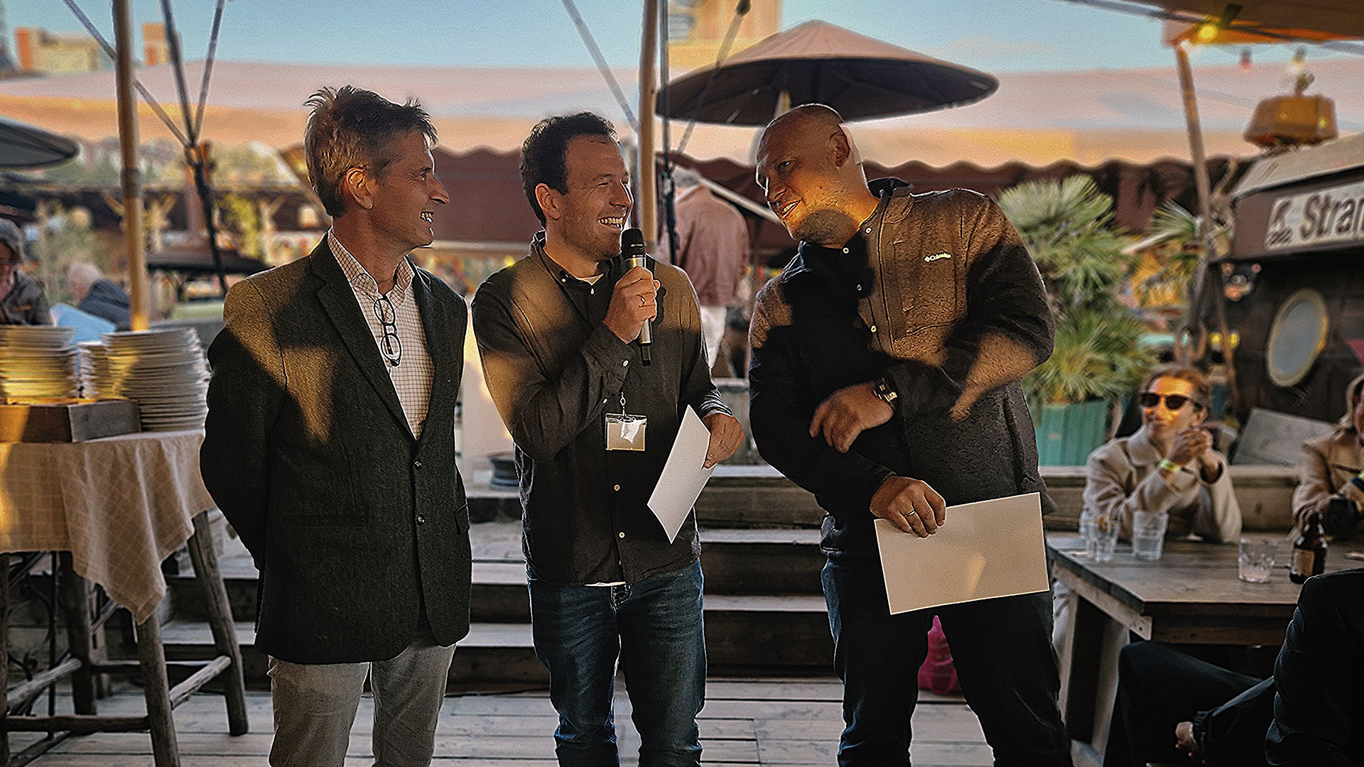 Three people standing on a patio, the one in the middle (Christoph Drobner) presenting his prize certificate.